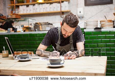 Young male cafe owner doing paperwork at table View Large Photo Image Stock Photo - Young male cafe owner doing paperwork at table. Fotosearch
