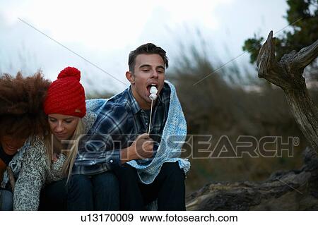 Young man and girlfriend eating toasted marshmallows on beach at dusk View Large Photo Image Stock Photo - Young man and girlfriend eating toasted marshmallows on beach at dusk. Fotosearch