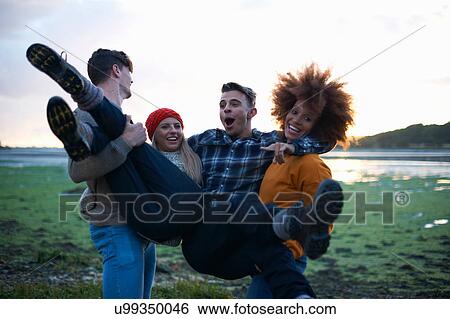 Stock Photograph - Young man and woman carrying friends at seaside sunset. Fotosearch