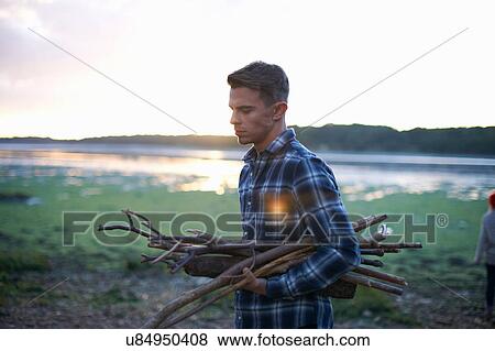 Stock Photo - Young man carrying sea driftwood at sunset. Fotosearch