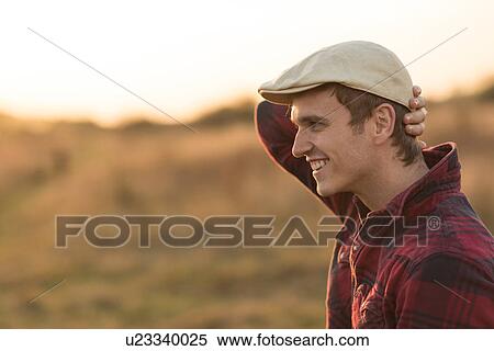 Stock Photography - Young man in rural setting, smiling, side view. Fotosearch