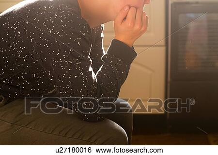 Stock Photograph - Young man indoors, sitting resting head on hand, mid section. Fotosearch