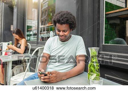 Young man looking at smartphone at city sidewalk cafe View Large Photo Image Stock Photo - Young man looking at smartphone at city sidewalk cafe. Fotosearch