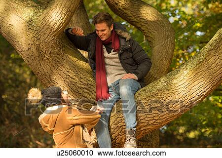 Young man sitting in tree, looking down at young woman on ground View Large Photo Image Stock Image - Young man sitting in tree, looking down at young woman on ground. Fotosearch