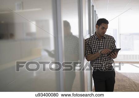 Stock Image - Young man standing in corridor with digital tablet. Fotosearch