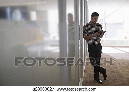 Stock Photo - Young man standing in corridor with digital tablet. Fotosearch