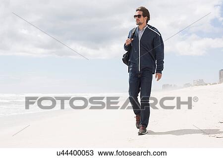 Stock Image - Young man strolling alone on beach, Western Cape, South Africa. Fotosearch