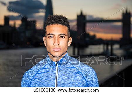 Stock Image - Young man, Tower Bridge in background, Wapping, London, UK. Fotosearch