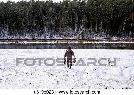 Young man walking through snow towards lake, rear view View Large Photo Image Stock Image - Young man walking through snow towards lake, rear view. Fotosearch
