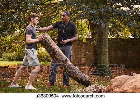 Young man with personal trainer lifting tree trunk in park View Large Photo Image Picture - Young man with personal trainer lifting tree trunk in park. Fotosearch