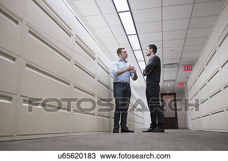 Stock Image - Young men talking to each other in corridor. Fotosearch