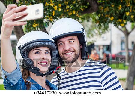 Stock Image - Young moped couple taking selfie in park, Split, Dalmatia, Croatia. Fotosearch