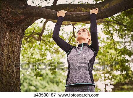 Stock Photo - Young woman doing pull ups on park tree branch. Fotosearch