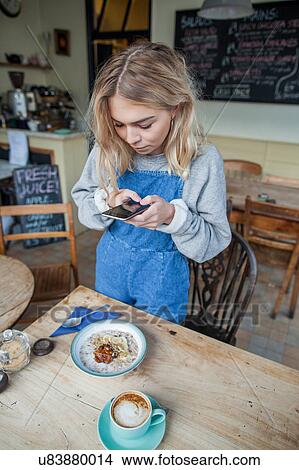 Picture - Young woman in cafe, using smartphone. Fotosearch