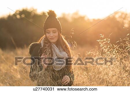 Stock Image - Young woman in field, looking at smartphone. Fotosearch