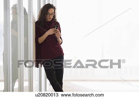 Young woman leaning on glass wall and text messaging View Large Photo Image Stock Image - Young woman leaning on glass wall and text messaging. Fotosearch