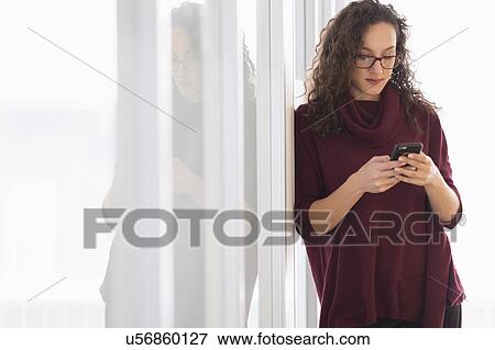 Stock Photo - Young woman leaning on glass wall and text messaging. Fotosearch