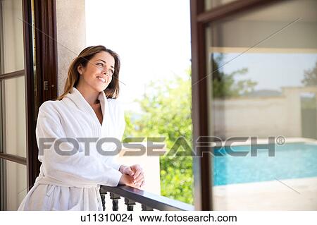 Picture - Young woman looking from window of boutique hotel suite, Majorca, Spain. Fotosearch
