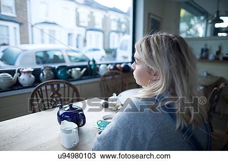 Young woman sitting in cafe, cup of tea and teapot on table, looking out of window View Large Photo Image Stock Image - Young woman sitting in cafe, cup of tea and teapot on table, looking out of window. Fotosearch
