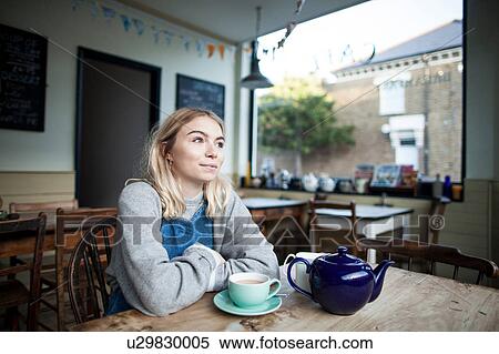 Young woman sitting in cafe, cup of tea and teapot on table, thoughtful expression View Large Photo Image Stock Photography - Young woman sitting in cafe, cup of tea and teapot on table, thoughtful expression. Fotosearch