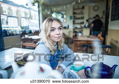 Stock Image - Young woman sitting in cafe, looking out of window. Fotosearch