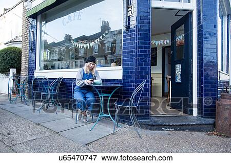 Stock Photo - Young woman sitting outside cafe, using smartphone. Fotosearch