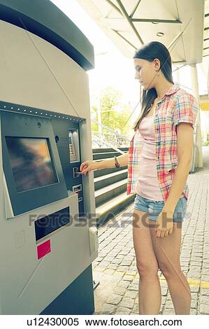 Stock Photography - Young woman using ticket machine. Fotosearch