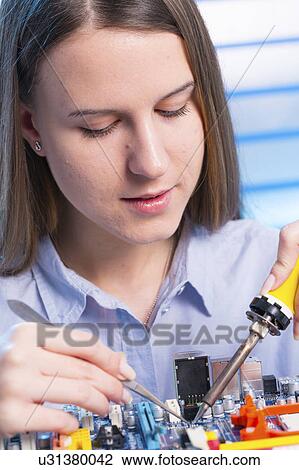 Stock Image - Young woman working on circuit board. Fotosearch