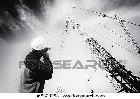 Stock Image - Engineer on cell phone pointing up towards a crane.. Fotosearch