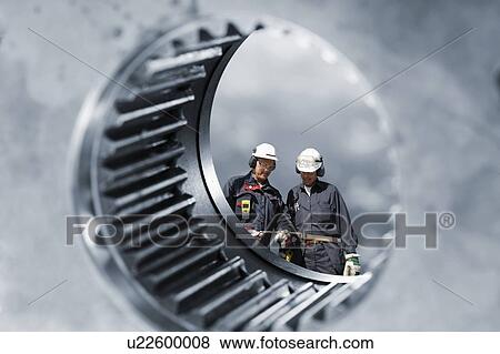 Stock Photo - MODEL RELEASED. Large gears with industrial workers.. Fotosearch