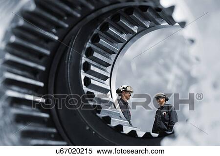 Stock Photography - MODEL RELEASED. Large gears with industrial workers.. Fotosearch