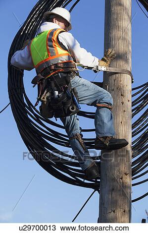 Stock Image - Cable lineman raising new cable up onto power pole. Fotosearch