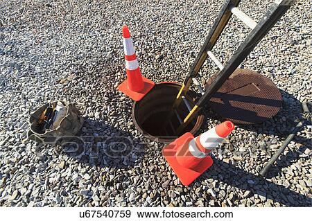 Stock Photo - Ladder in manhole and warning cones. Fotosearch