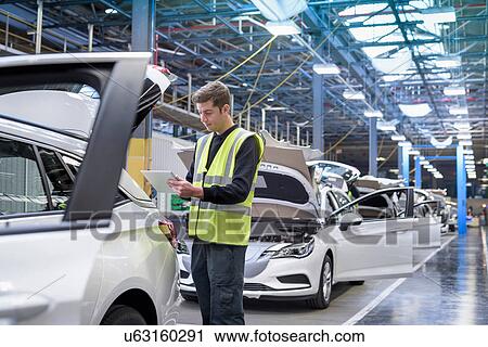 Stock Image - Apprentice car inspector using tablet in car factory. Fotosearch