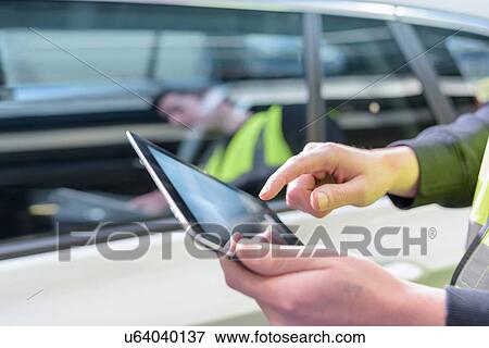 Stock Photo - Apprentice car inspector using tablet in car factory, close up. Fotosearch