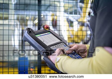 Stock Image - Apprentice engineer operating robots on production line in car factory, close up. Fotosearch