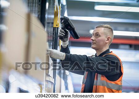 Stock Image - Apprentice scanning parts numbers in parts store in car factory. Fotosearch