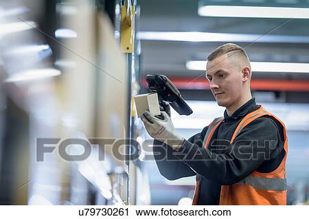 Stock Image - Apprentice scanning parts numbers in parts store in car factory. Fotosearch