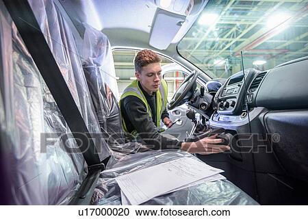 Stock Image - Apprentice vehicle inspector inspecting interior of vehicle in car factory. Fotosearch