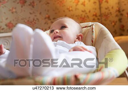 Stock Image - Baby girl lying on baby bouncer chair in nursery. Fotosearch