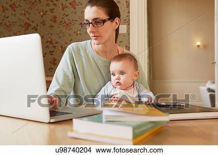 Picture - Baby girl sitting on mother's lap staring at laptop. Fotosearch