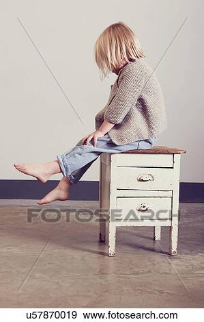 Stock Photo - Blond girl sitting on old cabinet looking down. Fotosearch