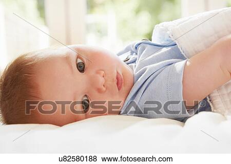 Stock Photo - Blue eyed baby boy lying on back on bed. Fotosearch