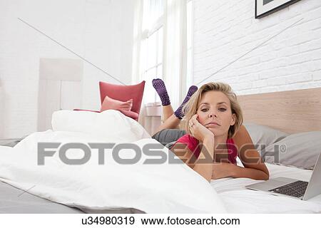Bored mid adult woman lying on bed by laptop View Large Photo Image Stock Photo - Bored mid adult woman lying on bed by laptop. Fotosearch