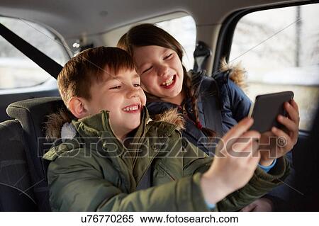 Stock Photography - Boy and sister taking laughing selfie in car backseat. Fotosearch