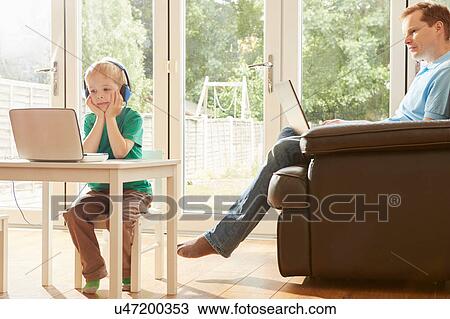 Boy at desk and father on sofa using laptops View Large Photo Image Stock Image - Boy at desk and father on sofa using laptops. Fotosearch