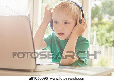 Stock Photography - Boy at desk using laptop and listening to headphones. Fotosearch