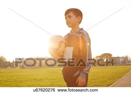 Boy football player holding ball in sunlit park View Large Photo Image Stock Photograph - Boy football player holding ball in sunlit park. Fotosearch