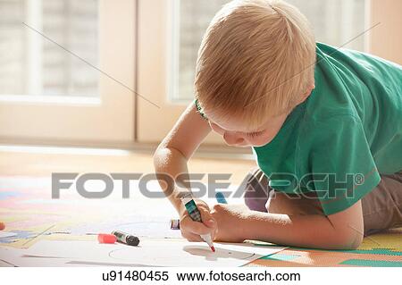 Stock Photography - Boy kneeling on floor drawing on paper. Fotosearch