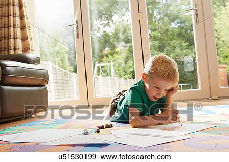 Stock Photo - Boy lying on floor drawing on paper. Fotosearch